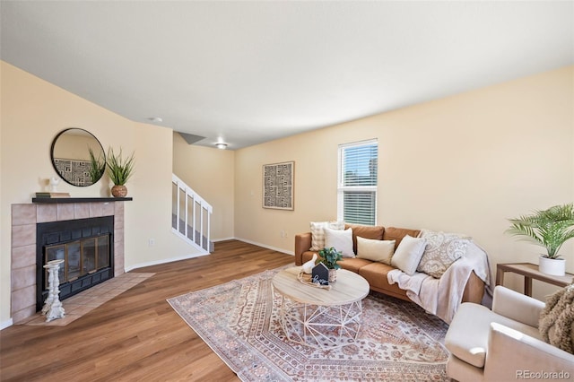 living room with stairs, a fireplace, baseboards, and wood finished floors