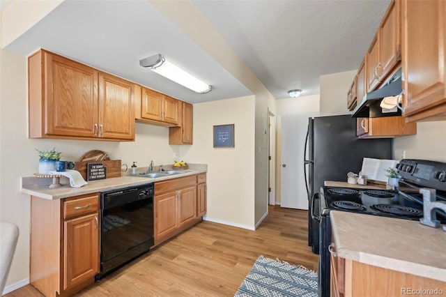 kitchen with a sink, light countertops, under cabinet range hood, black appliances, and light wood-style flooring