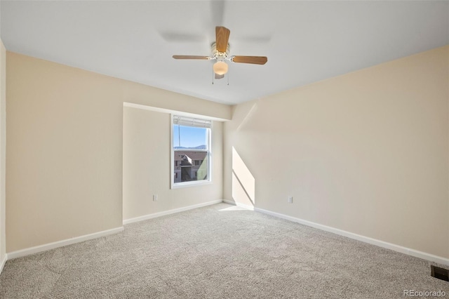 carpeted spare room with visible vents, baseboards, and a ceiling fan