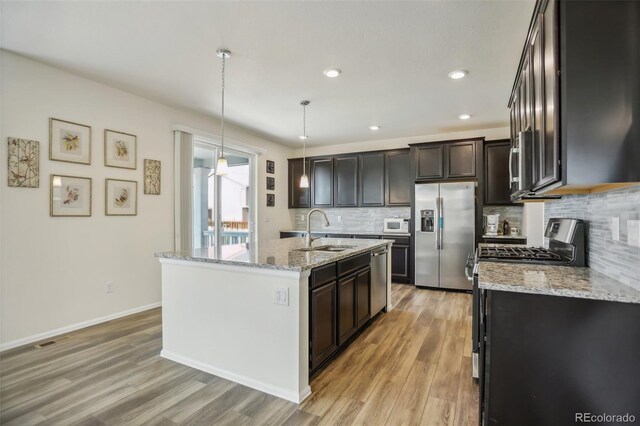 kitchen featuring light hardwood / wood-style flooring, tasteful backsplash, appliances with stainless steel finishes, sink, and a center island with sink