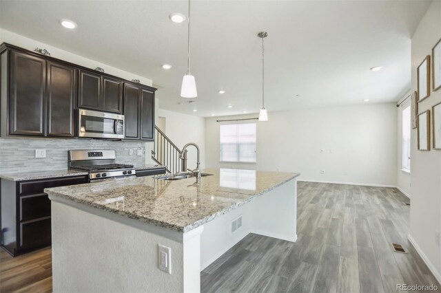 kitchen featuring appliances with stainless steel finishes, tasteful backsplash, hardwood / wood-style floors, a kitchen island with sink, and light stone countertops