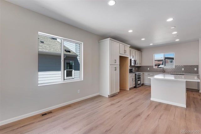 kitchen with white cabinetry, backsplash, stainless steel appliances, a kitchen island, and light wood-type flooring