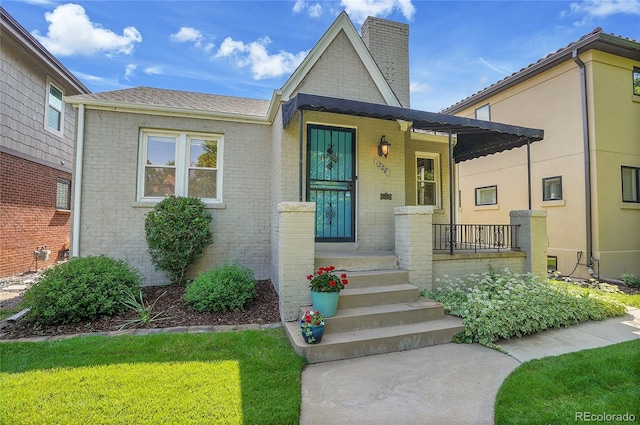 1208 S Elizabeth St, Denver, CO 80210 - view of front facade featuring a chimney, brick siding, roof with shingles, and a front yard