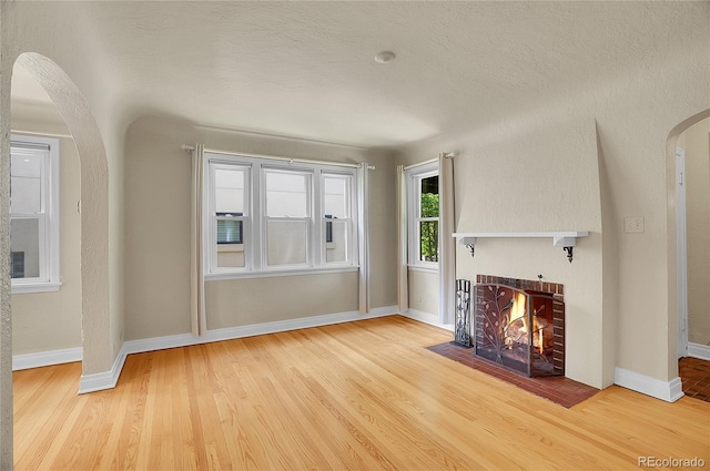 1208 S Elizabeth St, Denver, CO 80210 - unfurnished living room featuring arched walkways, a fireplace, wood finished floors, and baseboards
