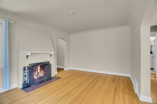 1208 S Elizabeth St, Denver, CO 80210 - unfurnished living room featuring arched walkways, a tiled fireplace, wood finished floors, and baseboards