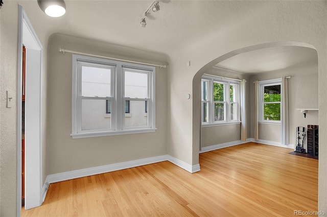 1208 S Elizabeth St, Denver, CO 80210 - unfurnished living room with arched walkways, light wood finished floors, baseboards, and track lighting