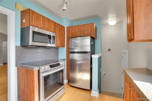 1208 S Elizabeth St, Denver, CO 80210 - kitchen featuring appliances with stainless steel finishes, light wood-type flooring, brown cabinets, tasteful backsplash, and baseboards