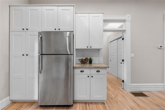 328 E Dakota Ave, Denver, CO 80209 - kitchen featuring freestanding refrigerator, light wood finished floors, white cabinets, tasteful backsplash, and light stone countertops