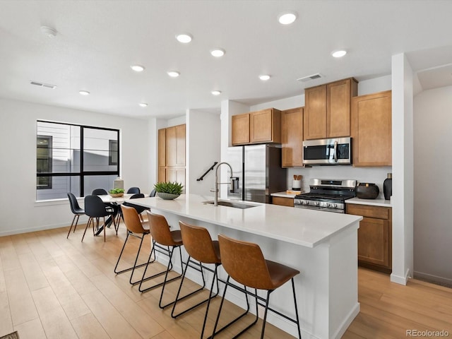 2050 S Holly St Unit 1, Denver, CO 80222 - kitchen featuring appliances with stainless steel finishes, light wood-type flooring, a kitchen bar, light countertops, and an island with sink