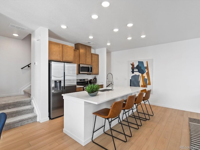 2050 S Holly St Unit 1, Denver, CO 80222 - kitchen featuring appliances with stainless steel finishes, a kitchen bar, light wood-type flooring, brown cabinetry, and an island with sink