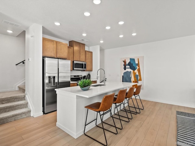 2050 S Holly St Unit 1, Denver, CO 80222 - kitchen featuring appliances with stainless steel finishes, light wood finished floors, a breakfast bar, a center island with sink, and recessed lighting