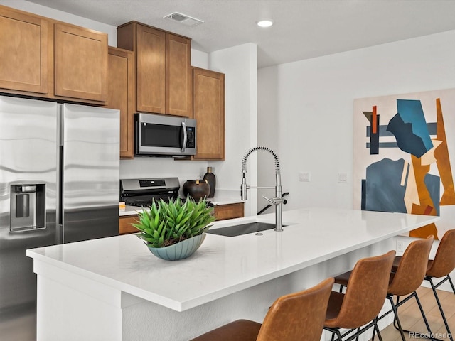2050 S Holly St Unit 1, Denver, CO 80222 - kitchen with appliances with stainless steel finishes, a breakfast bar area, light countertops, recessed lighting, and brown cabinetry