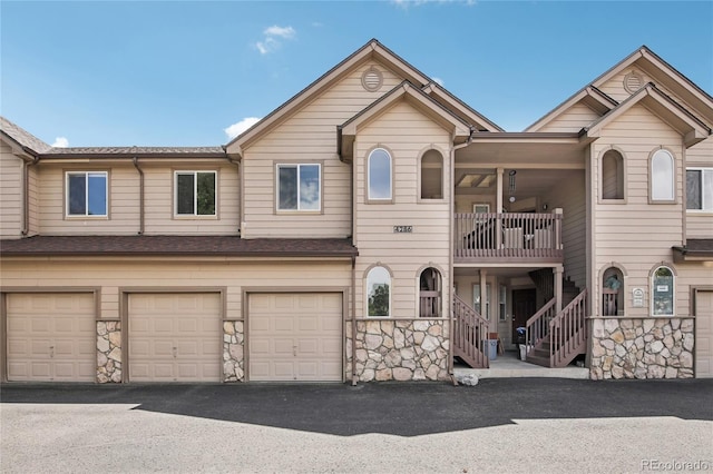 townhome / multi-family property featuring a garage, stone siding, driveway, and stairway