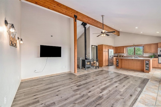 unfurnished living room with a wood stove, beam ceiling, light hardwood / wood-style floors, sink, and ceiling fan