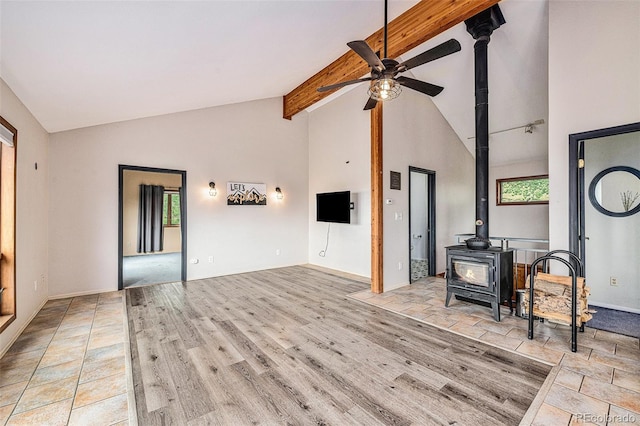 unfurnished living room featuring a wood stove, beam ceiling, high vaulted ceiling, ceiling fan, and light wood-type flooring