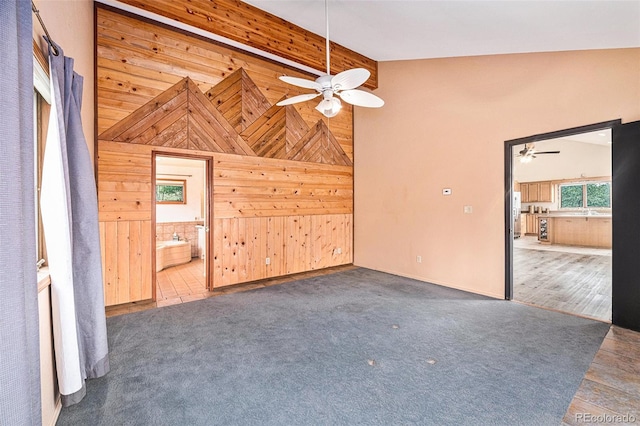 unfurnished living room with high vaulted ceiling, ceiling fan, hardwood / wood-style flooring, and wooden walls