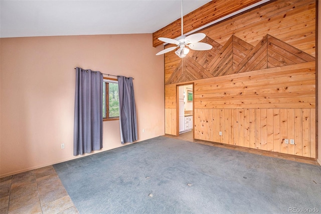 unfurnished living room with high vaulted ceiling, ceiling fan, wooden walls, and carpet floors