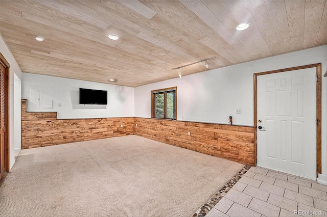 carpeted spare room with rail lighting, wood ceiling, and wooden walls