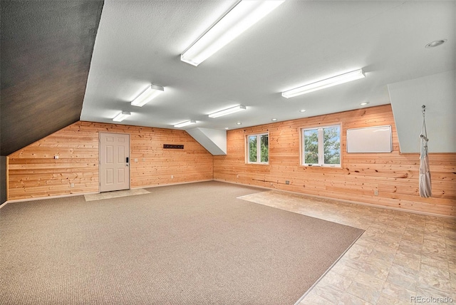 additional living space with a textured ceiling, wood walls, and lofted ceiling