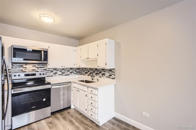 kitchen featuring light wood finished floors, a sink, decorative backsplash, light countertops, and appliances with stainless steel finishes