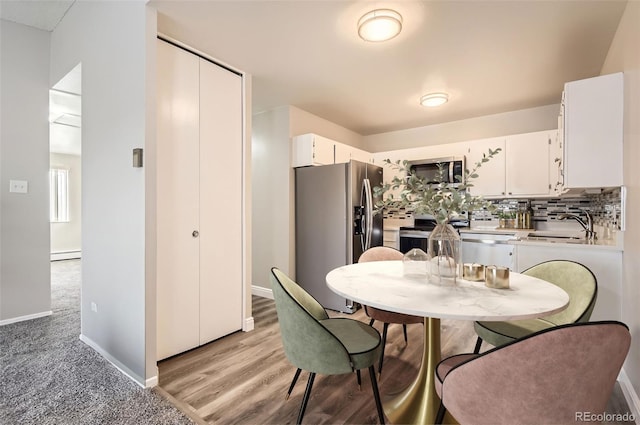 720 S Clinton St Unit 2D, Denver, CO 80247 - kitchen featuring a baseboard radiator, a sink, white cabinets, baseboards, and appliances with stainless steel finishes
