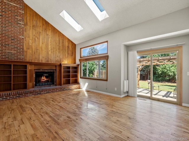 5903 S Ward St, Littleton, CO 80127 - unfurnished living room featuring high vaulted ceiling, a skylight, a brick fireplace, wood finished floors, and wooden walls
