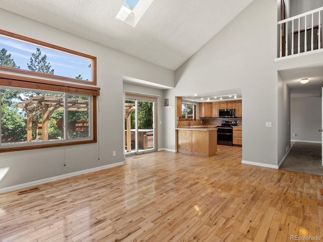5903 S Ward St, Littleton, CO 80127 - unfurnished living room featuring light wood finished floors, a towering ceiling, and a skylight
