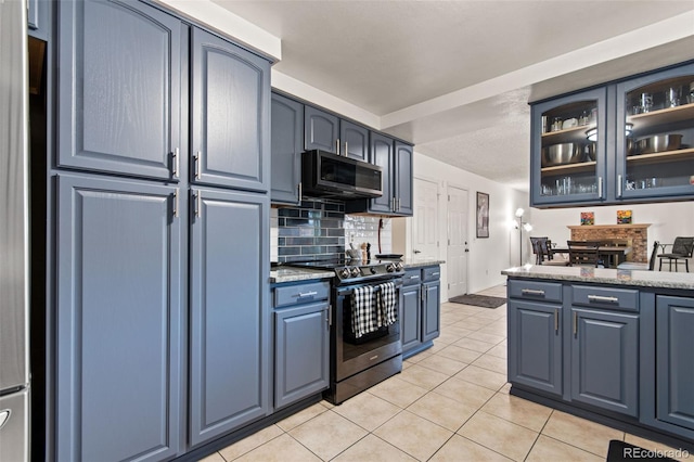 kitchen with light tile patterned floors, blue cabinetry, appliances with stainless steel finishes, backsplash, and light stone countertops