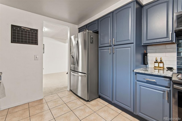 kitchen featuring blue cabinetry, appliances with stainless steel finishes, tasteful backsplash, light stone counters, and light tile patterned flooring