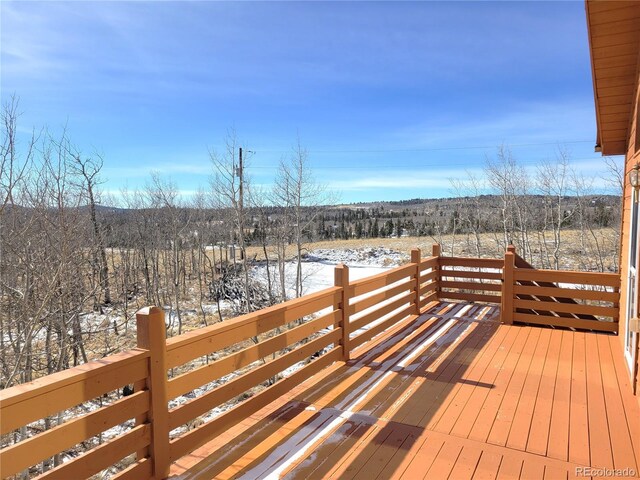 snow covered deck featuring a wooded view