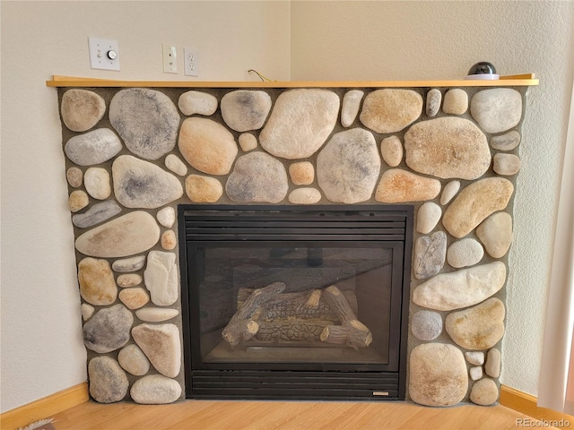 interior details featuring a stone fireplace, baseboards, and wood finished floors