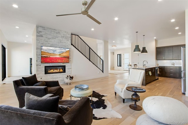 living room featuring recessed lighting, stairway, a stone fireplace, light wood finished floors, and ceiling fan