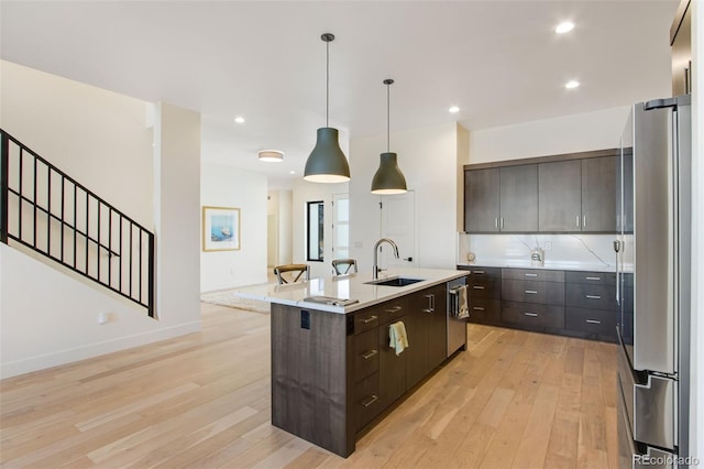 kitchen featuring light wood finished floors, dark brown cabinetry, light countertops, appliances with stainless steel finishes, and a sink