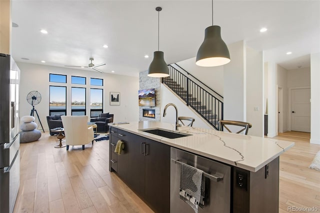 kitchen featuring light wood-type flooring, stainless steel refrigerator with ice dispenser, a sink, open floor plan, and a stone fireplace