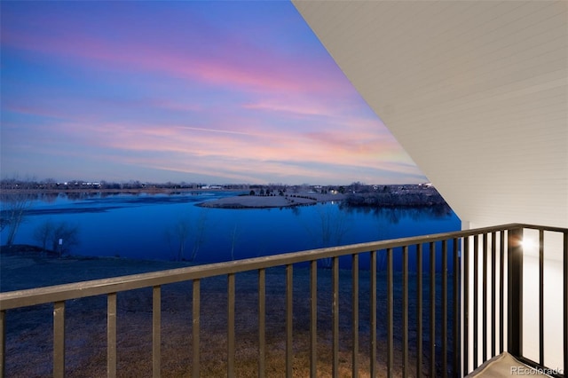 balcony at dusk featuring a water view