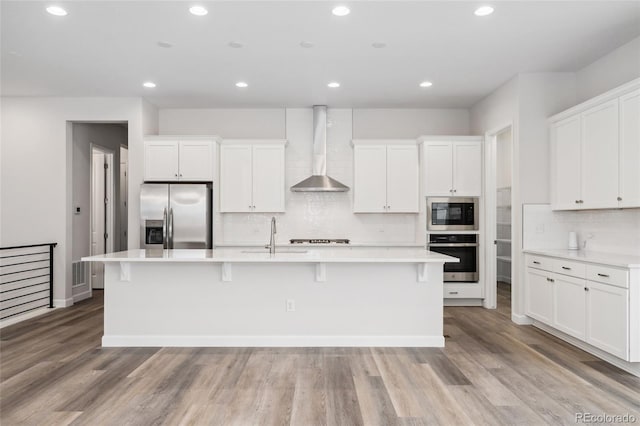 7051 S White Crow Way, Aurora, CO 80016 - kitchen featuring stainless steel appliances, wall chimney exhaust hood, a center island with sink, white cabinets, and tasteful backsplash