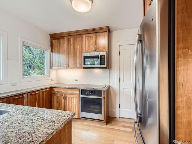 1453 Vine St, Denver, CO 80206 - kitchen featuring stainless steel appliances, brown cabinets, light stone countertops, and light wood-style flooring