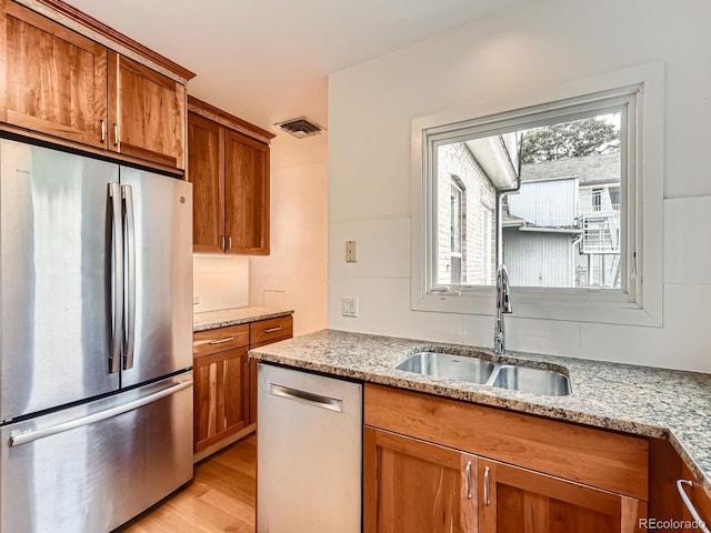 1453 Vine St, Denver, CO 80206 - kitchen with appliances with stainless steel finishes, a sink, brown cabinetry, light stone countertops, and light wood-style floors