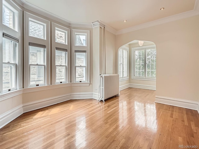1453 Vine St, Denver, CO 80206 - empty room with radiator heating unit, light wood-type flooring, arched walkways, and ornamental molding