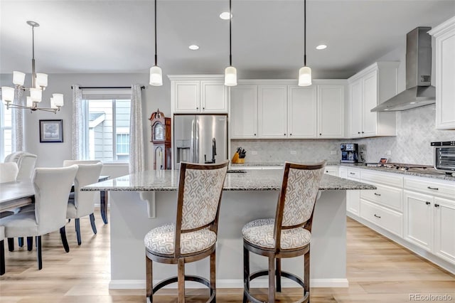 9055 Swan River St, Littleton, CO 80125 - kitchen with wall chimney range hood, stainless steel appliances, decorative backsplash, a chandelier, and a center island