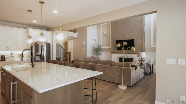 kitchen with sink, decorative light fixtures, dark hardwood / wood-style floors, an island with sink, and white cabinets