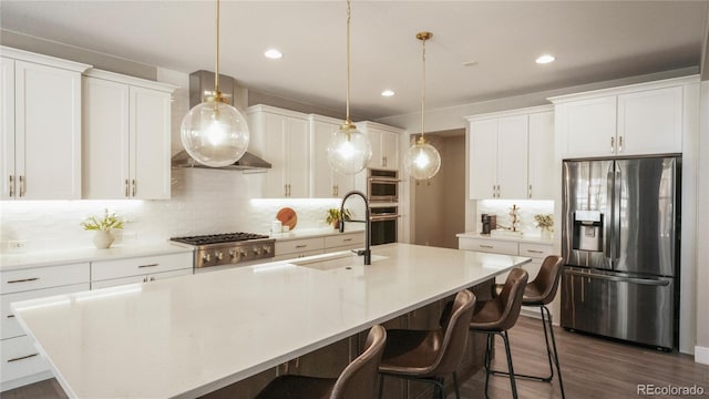 kitchen featuring stainless steel appliances, hanging light fixtures, a kitchen island with sink, and white cabinets