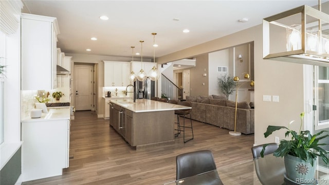 kitchen featuring sink, wood-type flooring, white cabinets, a center island with sink, and decorative light fixtures