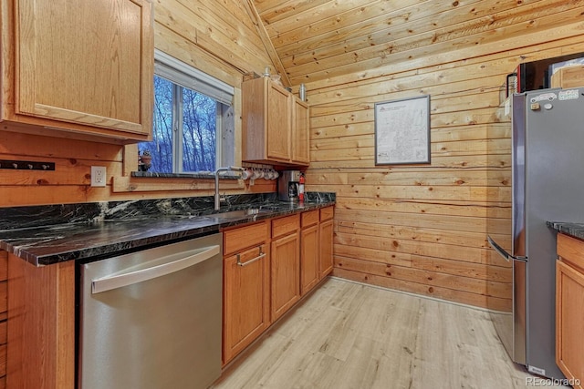 kitchen with a sink, light wood-style floors, appliances with stainless steel finishes, wood walls, and lofted ceiling