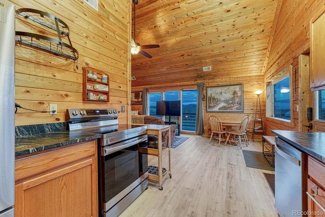 kitchen with wooden walls, light wood-type flooring, a towering ceiling, stainless steel appliances, and a ceiling fan