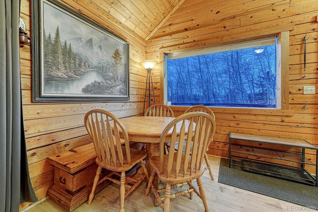 dining room featuring vaulted ceiling, wood finished floors, and wood walls