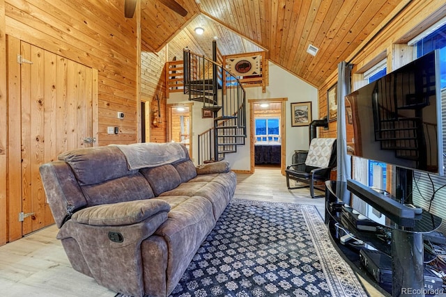 living area with wooden walls, wood finished floors, high vaulted ceiling, stairs, and wooden ceiling