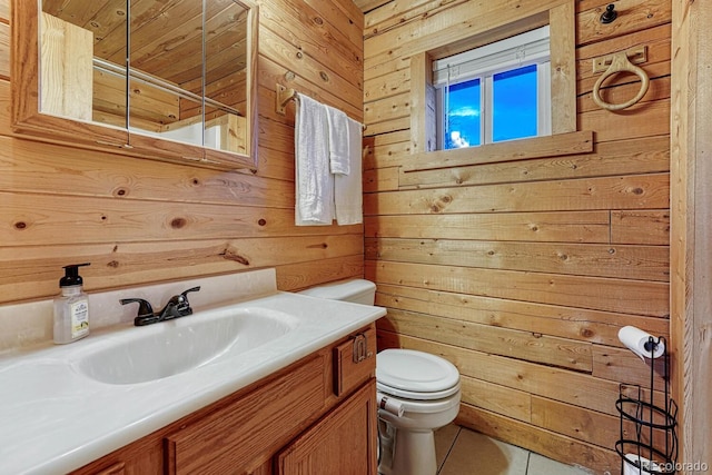 half bath with toilet, wood walls, vanity, and tile patterned flooring