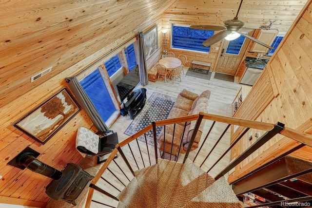 stairway with a ceiling fan, wood finished floors, wood walls, wood ceiling, and a wood stove