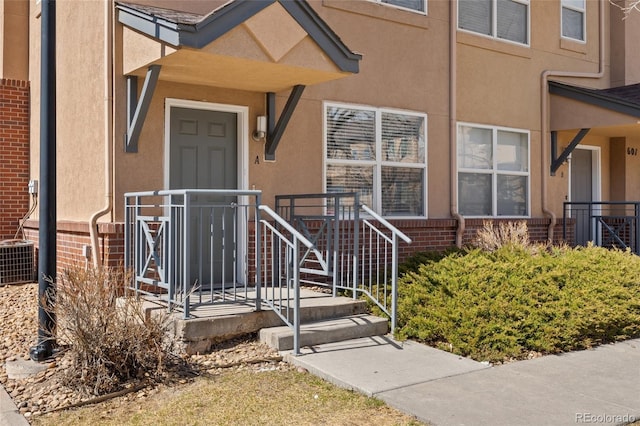 property entrance with central AC unit, brick siding, and stucco siding